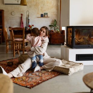 Happy young mother and toddler daughter spending time together on floor near fireplace at home. Cozy interior