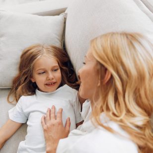 Mother and daughter sharing a tender moment on the couch, holding hands and smiling warmly at each other
